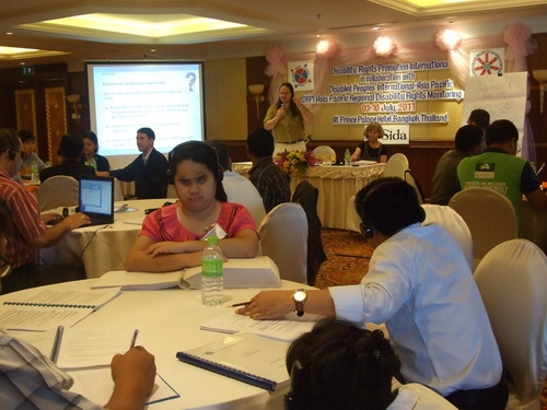 Nathan Bond stands and Marcia Rioux sits in the background while participants listen and work with training materials in the foreground. 