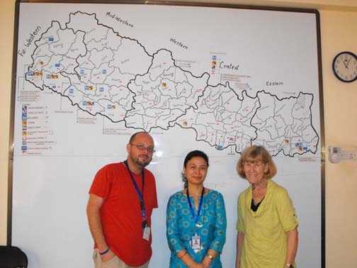 <p>Marcia Rioux poses with two staff persons from Handicap International, Nepal in front of a white board with a map.</p>
