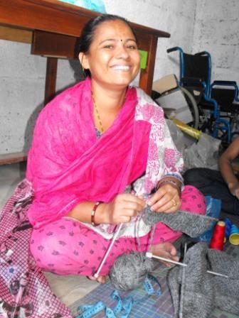 <p>Woman from Entire Power in Social Action, a disabled women&#39;s organization, sitting crossed legged working on a knitting project and smiling at the camera.</p>
