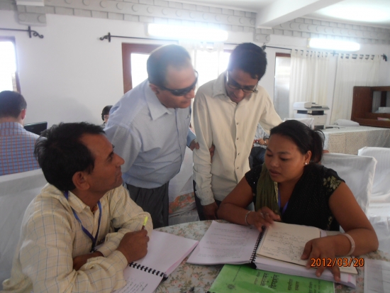 Ram is assisting with a discussion held by Mr. Birendra and two participants. Ram and Mr. Birendra are standing and the other two participants are seated. 