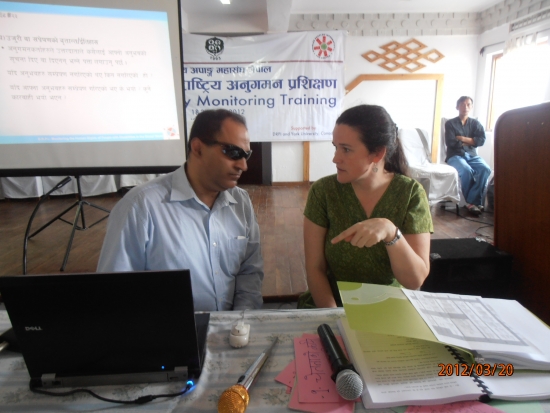 Mr. Birendra (left) and Rita Samson (right) sit as Rita makes a point with her arm raised to point at the computer in front of them. They are facing each other. 