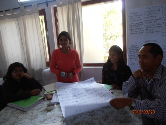 Four participants present their discussion results to the rest of the training group. Three are seated around a table and one is standing as the representative for the group. 