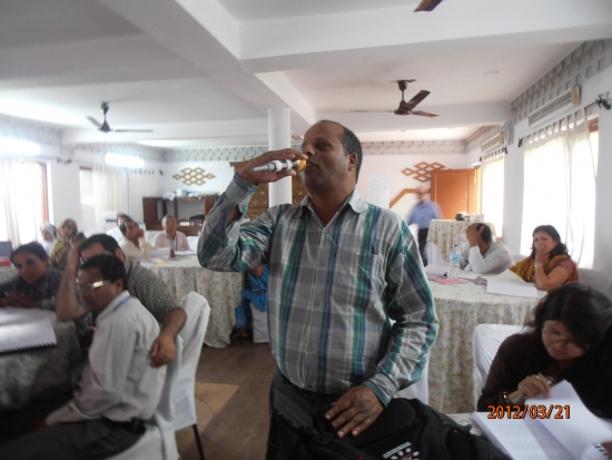 A participant stands as he adds to the discussion. He holds a micro phone in his right hand and he is holding it to his mouth. 