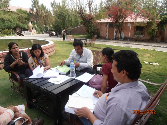 A group of participants sit in chairs in front of an ornamental pond and review their training manuals. 