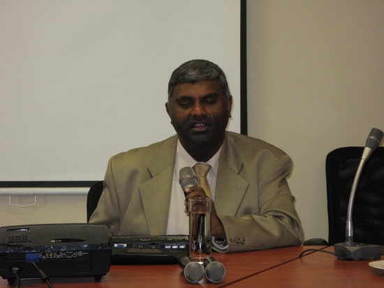 <p>
	Jace Nair is sitting at a table, speaking into a microphone.</p>

