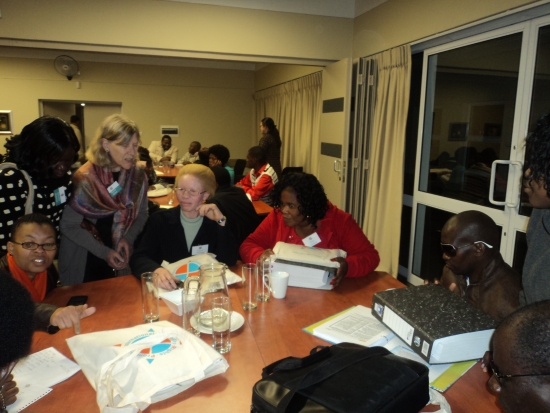 PMarcia is standing near Phumla Dydyo, Zama Ngwenya, Judith Madi, and Mnikelwa Nompilwane, who are sitting at a table in the training venue.