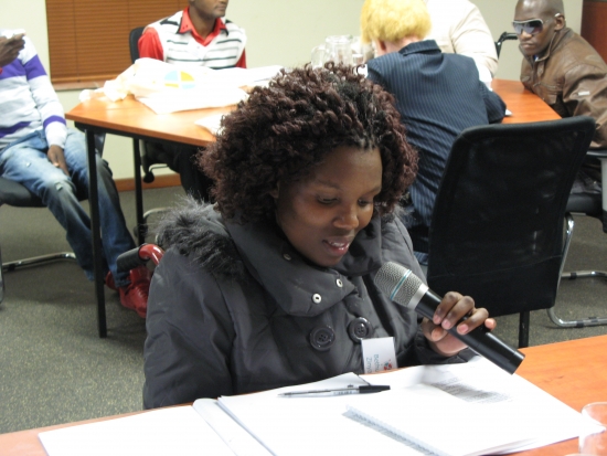 Bethulisile Zinyane holds a microphone during the session, while seated at a table looking down at her papers. 