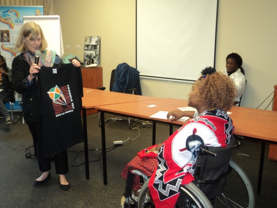 <p>
	Prof. Marcia Rioux is showing a T-shirt to Bongiwe Malope as a sign of her gratitude for organizing the workshop successfully. They are in front of a table and there is a white screen on the wall in the background.</p>
