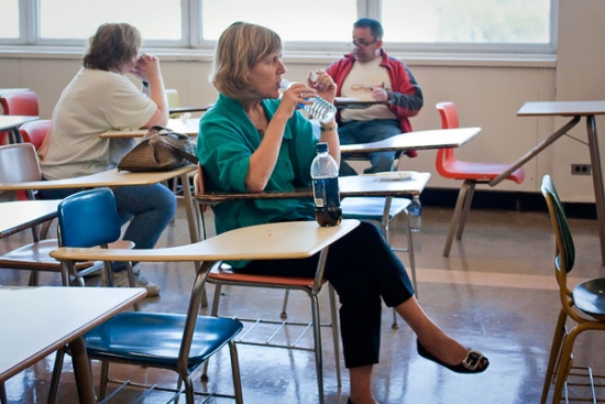 Marcia Rioux is seated at a desk and drinking water from a plastic water bottle.