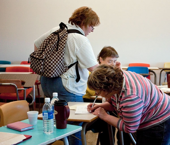 <p>
	Mary Anthony is bending down to fill out interview forms on a desk.</p>
