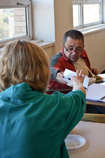 Marcia Rioux and Steve Estey are sitting across a table from each other and exchanging a paper and pen.