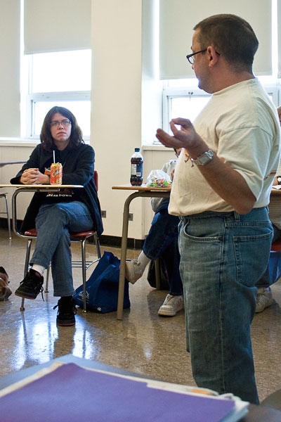 Steve Estey is presenting in the foreground while Stephanie McGrath sits in a desk listening.