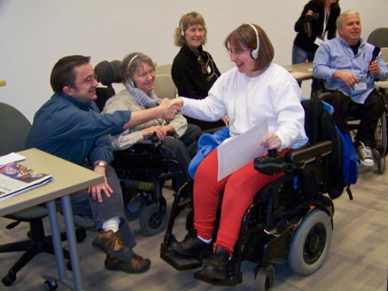 Participant Robin smiles broadly while holding a certificate and shaking hands with Steve Estey.