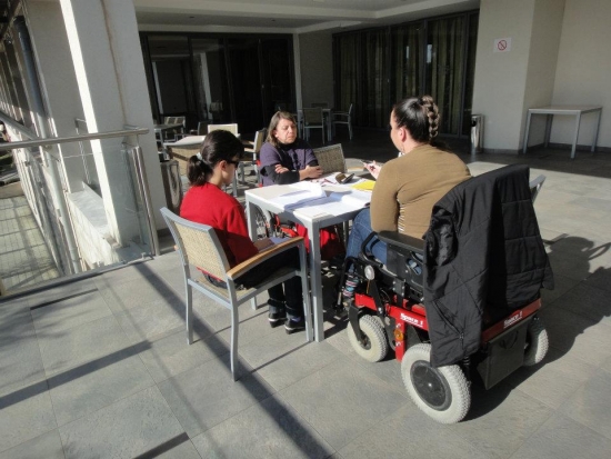 Seated outside at  a table in the sun light practicing during the country monitoring training in Montenegro. 