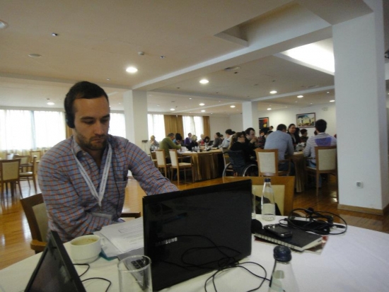 Chris is sitting off to the side during a presentation with headphones on as he listens to translation from across the room.