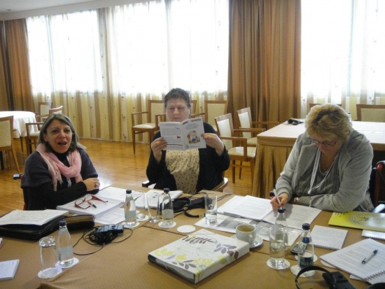 Three participants are gathered around a table, one participant looks down at her notes.