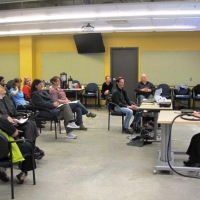 <p>
	Participants listen while Laura Mackenrot presents at a desk at the front of the room.</p>
