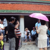 Participants and facilitators sit and stand by the steps of the Grand Palace while listening to a tour guide.