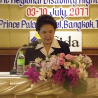 Ms. Kingkaew Inwang sits at a table and speaks into a microphone.