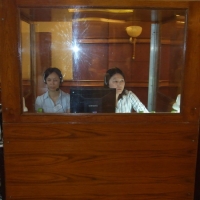 Two women sit in an enclosed booth with headphones on their heads. 