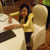 Phoutsady Laoly smiles and while sitting at a table and writing in a notebook. 