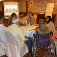 <p>
	Participants and facilitators sit and talk around a large round table.</p>
