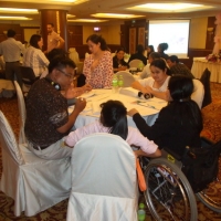 Chona Sabo stands beside a table of seated participants during training.