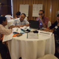 Ms. Ram, Mr. Birendra, Mr. Harka and Mr. Chintamani sit around a table working with training materials. 