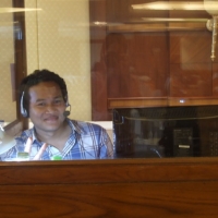 Sawang Srisom sits alone in an enclosed booth and smiles. 