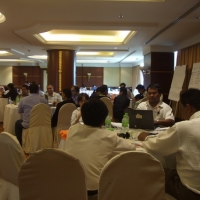 Many participants are seen sitting at tables and working with training materials. 