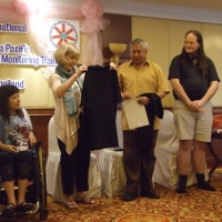 Lauro and Nathan stand while Marcia Rioux hands them t-shirts. Saowalak looks on.