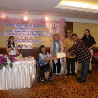 Kumar Regmi smiles and bends with arms outstretched holding his certificate with Saowalak Thonkuay. All the facilitators in the photo are laughing.