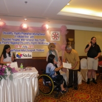 Lauro Purcil holds his certificate and shakes hands with Saowalak Thonkuay while other facilitators look on. 