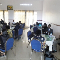 Participants sit in groups at small circular tables in a room with white walls.