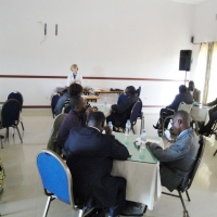 All participants are reading their materials, while Marcia Rioux speaks into a microphone.
