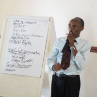 A man speaks into a microphone and stands beside a flip chart showing attitudes people have toward people with disabilities.