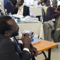 Mr. Tambo Camara sits and speaks to particpants using a microphone.