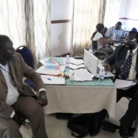 Mr. Mohamed Fall sits at a table with Tambo Camara at the  front. Mrs. Bongi Malope, Bruno Shyirambere and Sam Ntazinda Badege sitting behind in the corner.
