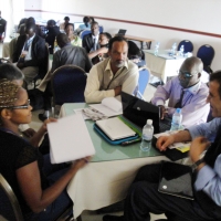 A woman and three men can be seen sitting around a table loaded with laptops and paper.