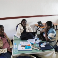 Three women sit around a table filled with laptops and training materials.