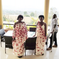 Mrs. Saphira Nyiransengimana and Apoche pose on a veranda at the centre of the photo, while Bruno Shyirambere looks on. 