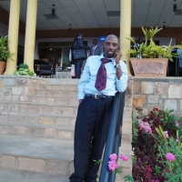 Mr. Ted Kaberuka talks on a phone while standing on stairs outside the hotel.