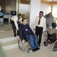 <p>
	A man pulls another in a wheelchair up a small section of stairs outside the training room while others watch.</p>
