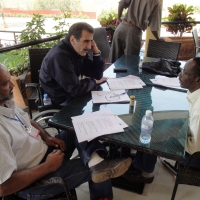 Three men sit at a table covered with training materials on a veranda.