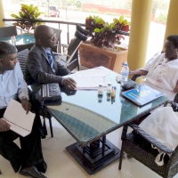 Magdalena Tiba Kaihuzi, Robert Mkozho and Jace Nair sit and talk at a table on a veranda.