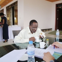 A man sits at a table with food in one hand and a cup in the other.