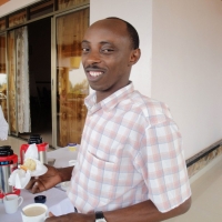 A man stands and smiles while holding food in one hand and a cup in the other