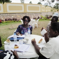 Roseweter Mudarikwa and Esther Kyozira and a couple of others sit outdoors at a round table and have a snack.