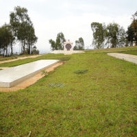 <p>
	A large grass covered area is shown with two large, white stone areas. In the distance a memorial marker and some trees can be seen.</p>
