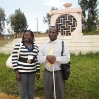 Felician Mkude (right) and Nancy Aswani Amwoso (left) stand in front of an outdoor monument to the genocide victims.
